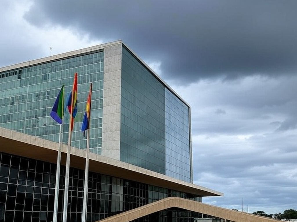 Edifício da CLDF em Brasília com bandeiras arco-íris sob céu nublado, representando programa para LGBTQIAPN+ com críticas de atraso.