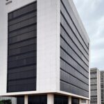 Edifício da Caesb em Brasília com papéis de resultados de concurso espalhados, simbolizando frustração de candidatos.