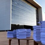 Fachada do TJDFT em Brasília com pilhas de processos judiciais, representando julgamento de 607 mil casos e alta demanda.