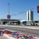 Rua festiva em Brasília no Carnaval 2026, com decorações e transporte gratuito, arquitetura icônica ao fundo.