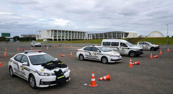 Viaturas policiais do DF em área de treinamento em Brasília, com equipamentos de segurança, sob céu nublado representando crise de criminalidade.