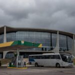 Fachada da Câmara Legislativa do DF com posto de gasolina e ônibus ao fundo, representando aprovação de meia-entrada seletiva e críticas orçamentárias.
