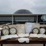 Plenário vazio da CLDF com documentos de seguros e relógio, simbolizando desperdício de tempo em homenagem questionável.