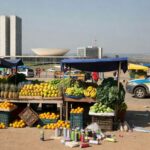 Viatura da PMDF em rua de Brasília com feira e ônibus ao fundo, representando detenção por uso de spray de gás.