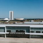 Hospital em Brasília com arquitetura icônica ao fundo, representando redirecionamento de R$ 25 milhões para saúde após cancelamento de comemorações.